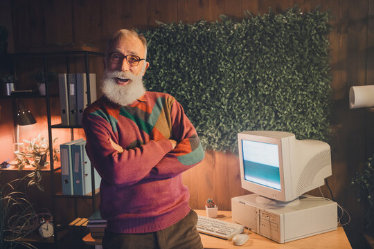Elderly male programmer working on vintage computer in cozy home office with a friendly smile reflecting a professional vibe