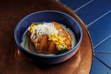 Gourmet croissant with creamy corn filling and parmesan cheese in blue bowl – elegant food presentation on rustic copper background