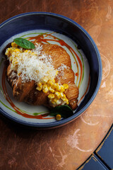 Gourmet croissant with creamy corn filling and parmesan cheese in blue bowl – elegant food presentation on rustic copper background