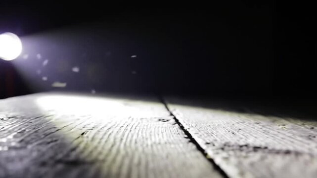Close-up of a textured wooden surface with dramatic lighting and lens flares against a dark background, The light from the lantern in the dusty room glides across the wooden surface of the old table