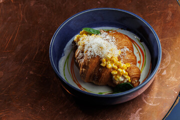Gourmet croissant with creamy corn filling in blue bowl – elegant food presentation on rustic copper background. close up