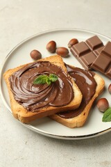 Toasts with tasty chocolate spread, pieces, mint and hazelnuts on light table, closeup