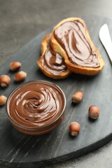 Tasty chocolate spread, toasts and hazelnuts on gray table, closeup