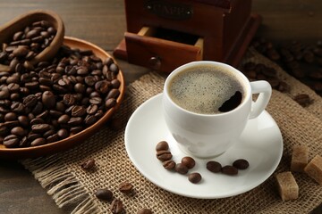 Aromatic coffee in cup, beans, brown sugar and grinder on wooden table, closeup