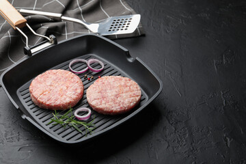Fresh raw patties for burger and spices in frying pan on black table, closeup. Space for text