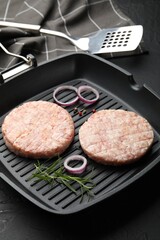 Fresh raw patties for burger and spices in frying pan on black table, closeup