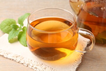 Aromatic lemon balm tea in glass cup, teapot and fresh leaves on wooden table, closeup