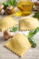 Uncooked ravioli, mushrooms and basil on white wooden table, closeup