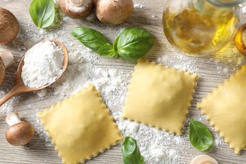 Uncooked ravioli, mushrooms and basil on white wooden table, flat lay