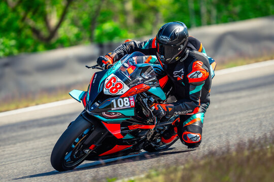  a person wearing a helmet, gloves, and shoes riding a 2018 Alpinestars Tech 3 motorcycle down a road surrounded by trees