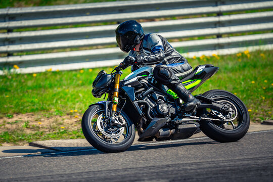  a person wearing a helmet, gloves, and shoes riding a Kawasaki Z900 motorcycle down a road surrounded by grass and flowers, with a railing in the background
