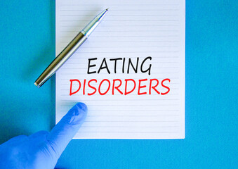 Eating disorders symbol. Concept words Eating disorders on beautiful white note. Doctor's hand in blue medical glove. Beautiful blue background. Medical healthy lifestyle eating disorders concept.