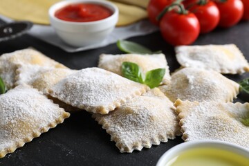 Uncooked ravioli, sauce, tomatoes and basil on black table, closeup