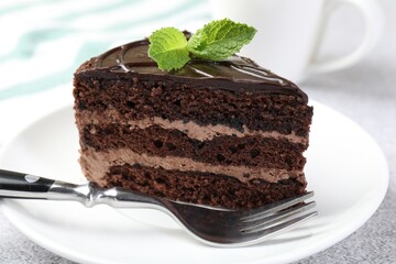 Piece of delicious chocolate cake with mint and fork on table, closeup