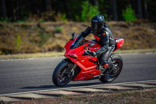  a person wearing a helmet, gloves, and shoes riding a red 2020 Ducati Panigale V4 S motorcycle down a road surrounded by trees and plants
