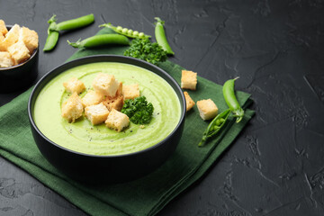Tasty pea cream soup with croutons and broccoli served on black table, closeup. Space for text