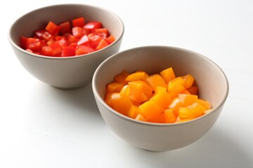 Pieces of fresh colorful bell peppers in bowls on white wooden table, closeup