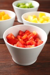 Pieces of fresh colorful bell peppers in bowls on wooden table, closeup