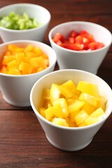 Pieces of fresh colorful bell peppers in bowls on wooden table, closeup