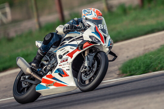  a person wearing a helmet, gloves, and shoes riding a BMW S1000RR motorcycle on a road surrounded by grass and poles, with a blurred background