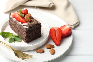 Piece of delicious chocolate cake with strawberries, almonds and mint on white wooden table, closeup
