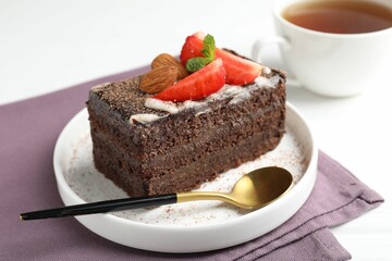 Piece of delicious chocolate cake with strawberry, almonds and tea on white table, closeup