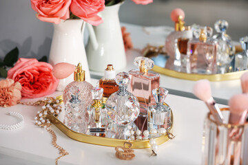 Bottles of different perfumes, accessories and flowers on dressing table indoors