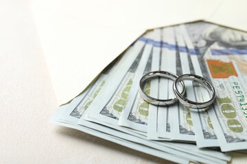 Two silver wedding rings, dollar banknotes and envelope on white table, closeup. Space for text