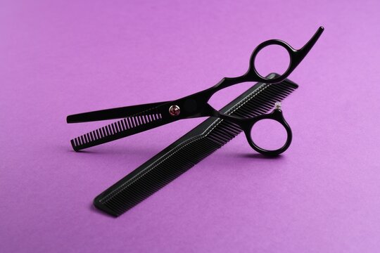Scissors and comb on violet background, closeup. Hairdresser's tools