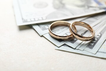 Two gold wedding rings and dollar banknotes on white table, closeup. Space for text