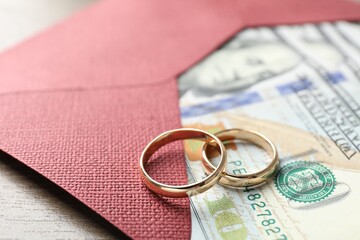 Gold wedding rings, envelope and dollar banknotes on wooden table, closeup