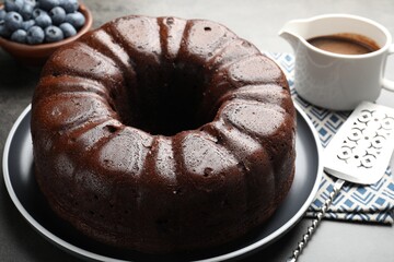 Tasty chocolate bundt cake, blueberries and server on grey table, closeup