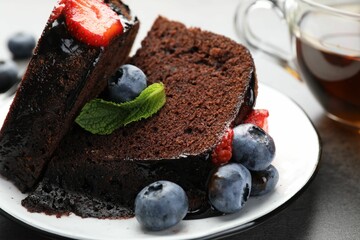 Pieces of delicious chocolate bundt cake with strawberries, mint and blueberries on grey table,...