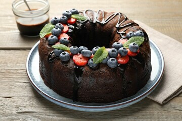 Delicious chocolate bundt cake with strawberries, mint and blueberries on wooden table, closeup