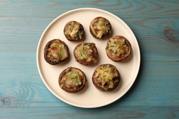 Delicious stuffed mushrooms with melted cheese and thyme on light blue wooden table, top view