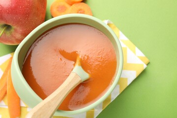Baby food. Tasty puree in bowl and ingredients on green background, above view. Space for text