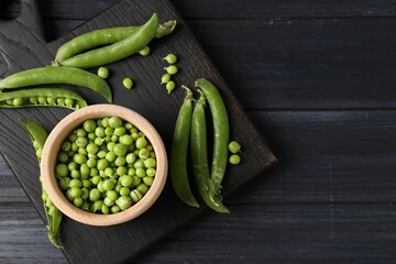 Fresh ripe green peas on black wooden table, flat lay. Space for text