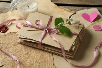 Stack of love letters, flower, paper hearts, candle and parchment sheets on wooden table, closeup