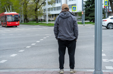 Man waiting at a crosswalk in a city setting with a bus approaching during the late afternoon