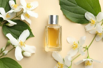 Bottle of perfume, beautiful jasmine flowers and green leaves on beige background, flat lay