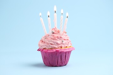 Burning candles in cupcake on light blue background