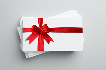 Gift card with red bow on light grey background, top view
