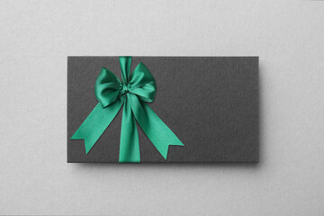 Blank gift card with green bow on light grey background, top view. Mockup for design