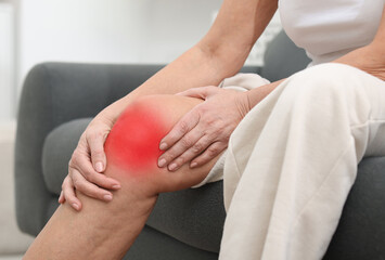 Senior woman suffering from pain in knee on sofa at home, closeup