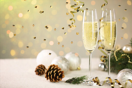 Sparkling wine, golden serpentine streamers, confetti and festive decor against blurred lights, space for text