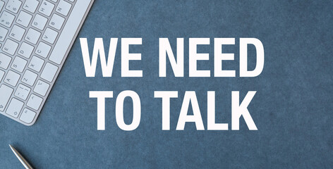 A keyboard and a pen are on a table with the words We need to talk written bel