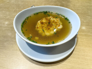 Delicious clear broth soup with herb and dumpling garnish on wooden table