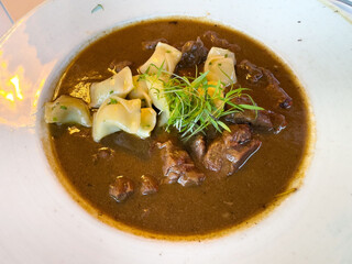 Savory beef stew with noodles and fresh herbs in white bowl