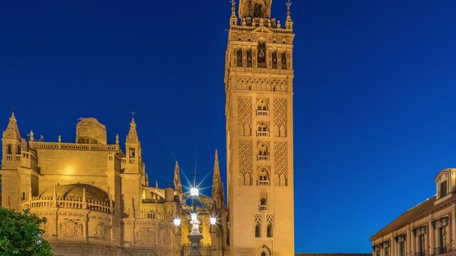 La Giralda and Seville Cathedral day to night transition timelapse, glowing with golden lights after sunset. The historic bell tower, gothic details and illuminated streets in Seville, Spain