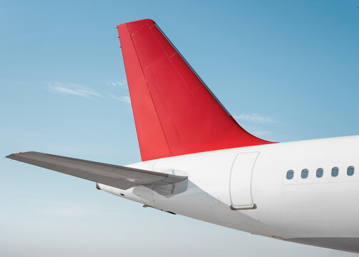 White airplane with tomato red tail against blue sky on a sunny day. Passenger aircraft's tail assembly on a clear blue sky background. 
